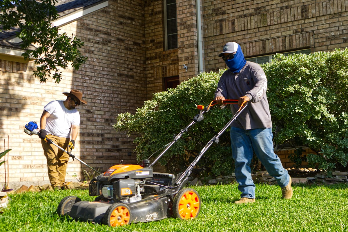 Two Evergreen Yard Works crew members mowing and trimming a residential lawn